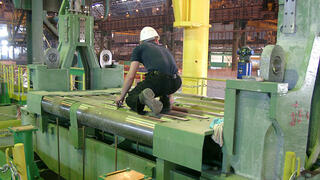 Stahlindustrie - Rollensegment. Ingenieur steht auf Rollensegment und tastet die Rollen mit einem Messtaster.